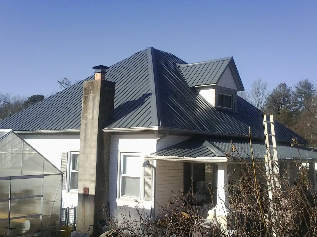 Dark blue standing seam metal roof on a white farmhouse with dormer — Slate & Tile Roof Repair by Roofing Brothers in Hertford