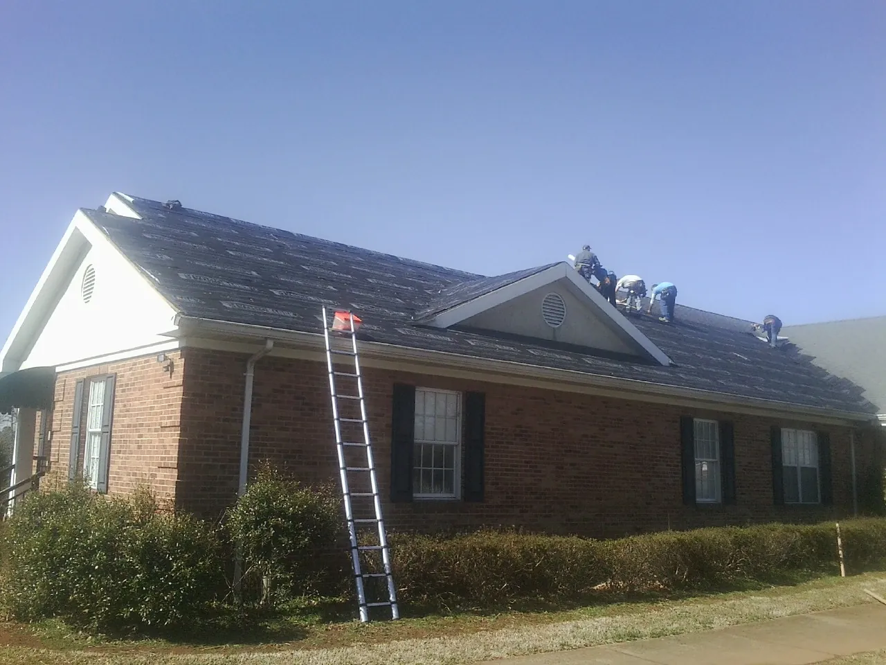 Crew tearing shingles off a brick ranch roof with a ladder set — Emergency Roof Repair work by our crew in Hertford