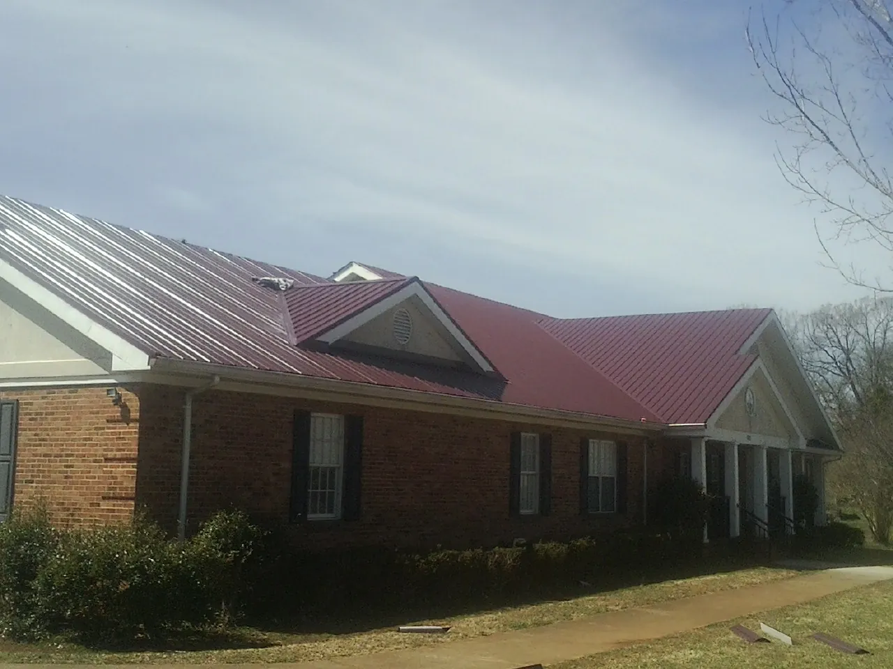 Red metal roof with gabled entries on a long brick building, from a Hail Damage Roof Repair job in Hertford