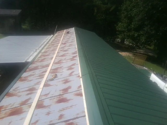 Old rusted panels beside newly installed green metal roofing — Wind Damage Roof Repair by Roofing Brothers in Hertford