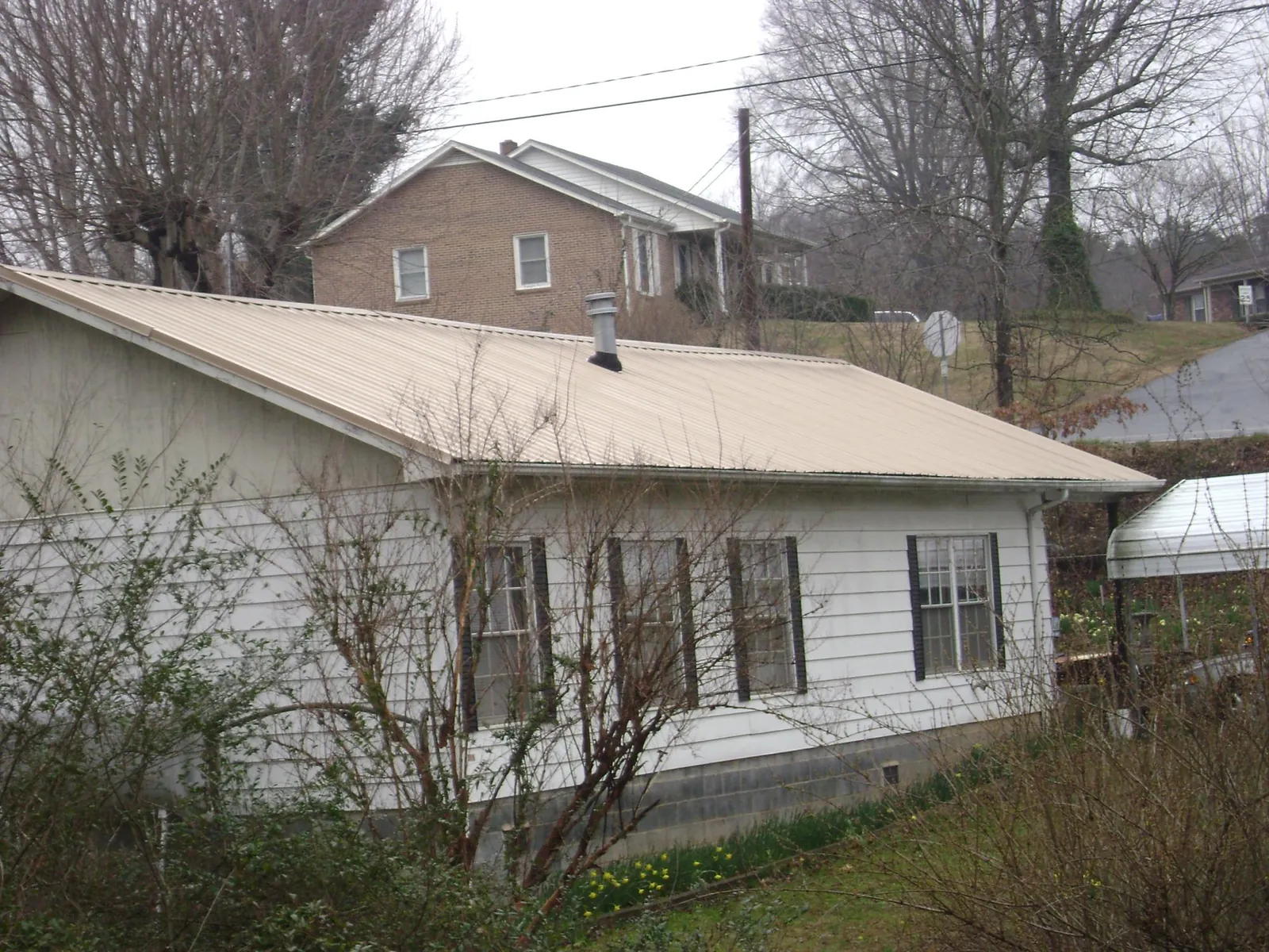 Tan metal roof on a white sided house set into a hillside — Commercial Roofing by Roofing Brothers in Hertford